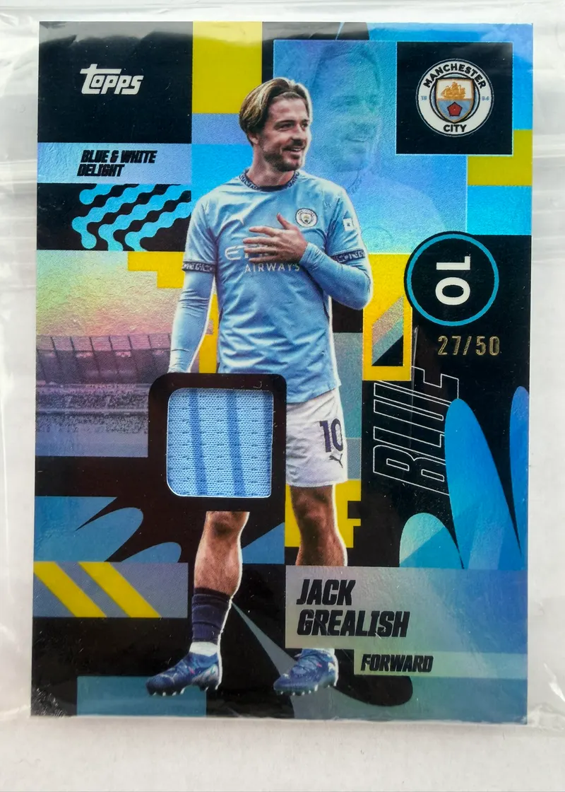 Jack Grealish, Topps Team Set Manchester City 2024/25 Blue & White Delight — awers z wszytym fragmentem koszulki i numeracją 27/50
