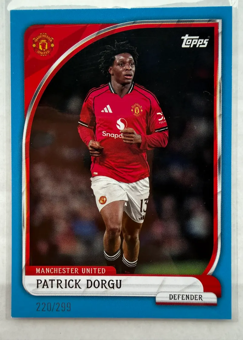 Patrick Dorgu, Topps Collector Tin Manchester United 2025/26, parallel Blue 220/299 — awers w niebieskiej ramce z zawodnikiem w czerwonym stroju United