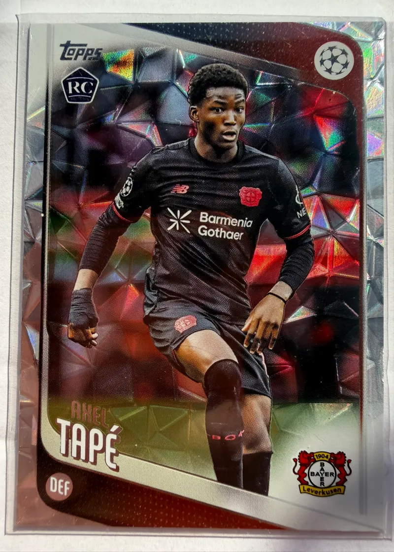Axel Tapé, Topps UEFA Club Competitions 2025/26 Diamante, karta 9 — awers z oznaczeniem RC, fasetowanym tłem i piłkarzem w czarnym stroju Bayeru Leverkusen
