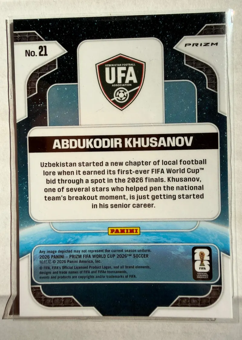 Abdukodir Khusanov, Panini Prizm FIFA World Cup 2026, karta 21 — rewers z herbem federacji Uzbekistanu i opisem pierwszego awansu na mundial