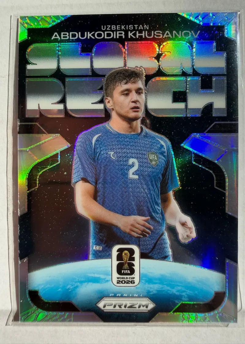 Abdukodir Khusanov, Panini Prizm FIFA World Cup 2026 Global Reach Silver Prizm, karta 21 — awers z napisem GLOBAL REACH, kulą ziemską u dołu i piłkarzem w niebieskim stroju reprezentacji Uzbekistanu z numerem 2